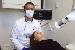 Sur la photo, David Côté montre ses nouveaux bras capteurs conçus pour aspirer les gouttelettes de salive près de la bouche des patients. Sa fille, Laurence, joue le rôle du patient. 
Photo : J-D Potié
